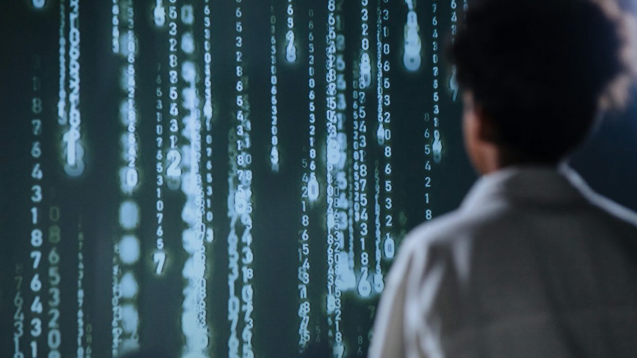 A person staring at a screen of binary code on a wall